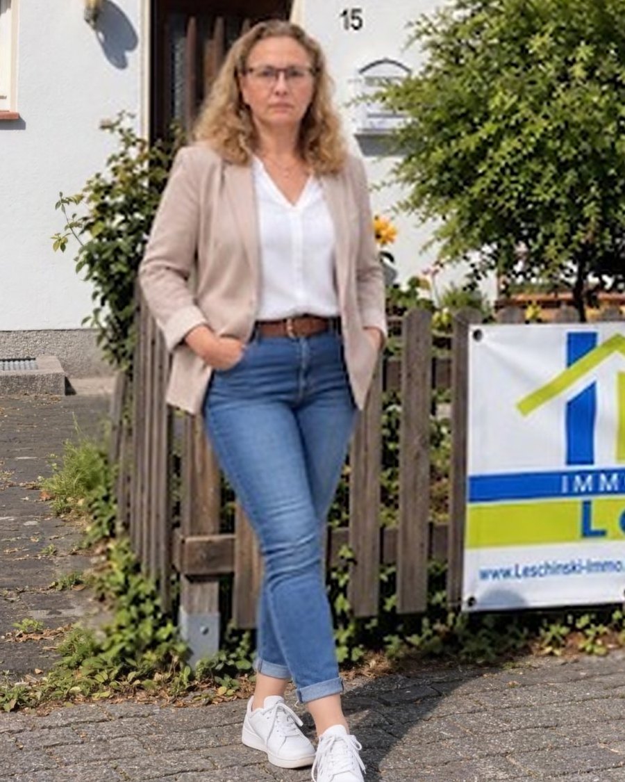 Daniela Leschinski vor einem Haus mit ihrem Schild „Zu verkaufen“